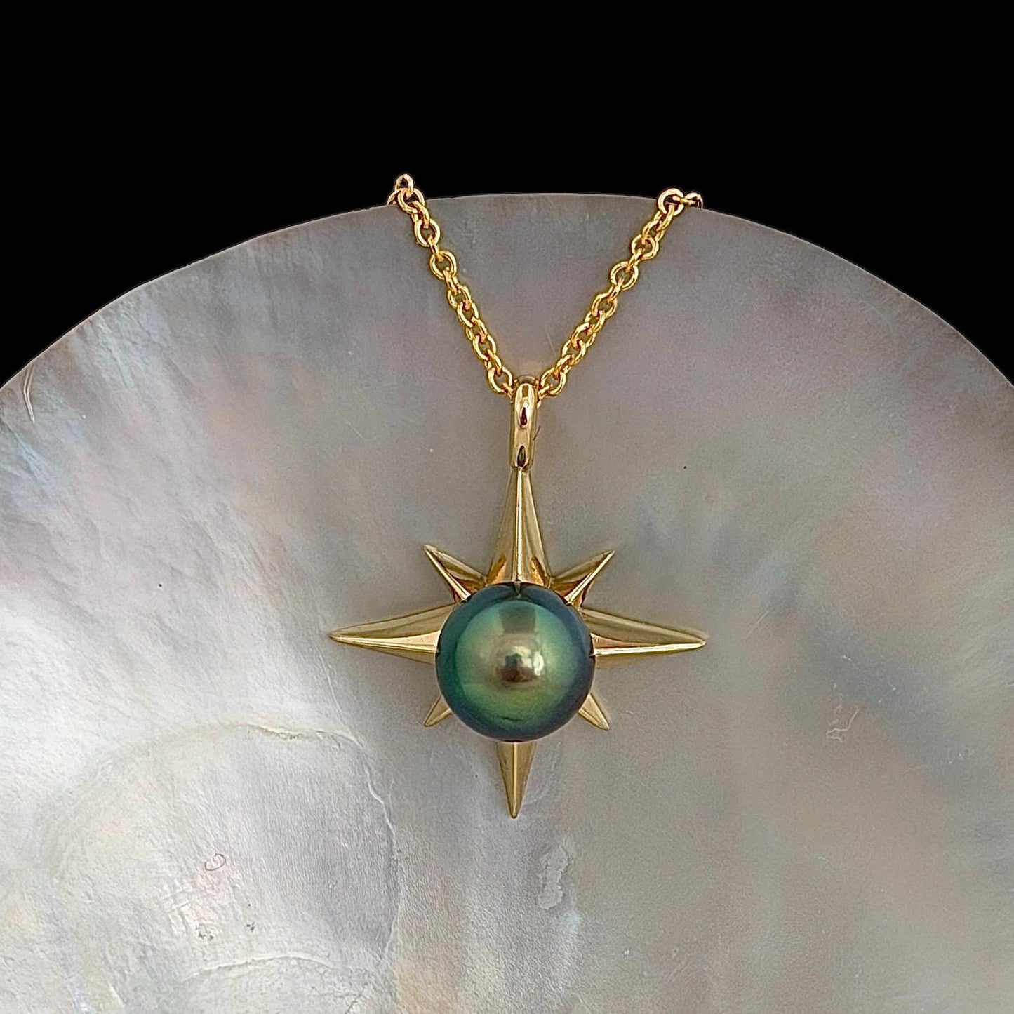 A gold-colored necklace featuring a starburst pendant with a vibrant blue green, round center stone. The pendant is suspended from a delicate chain.