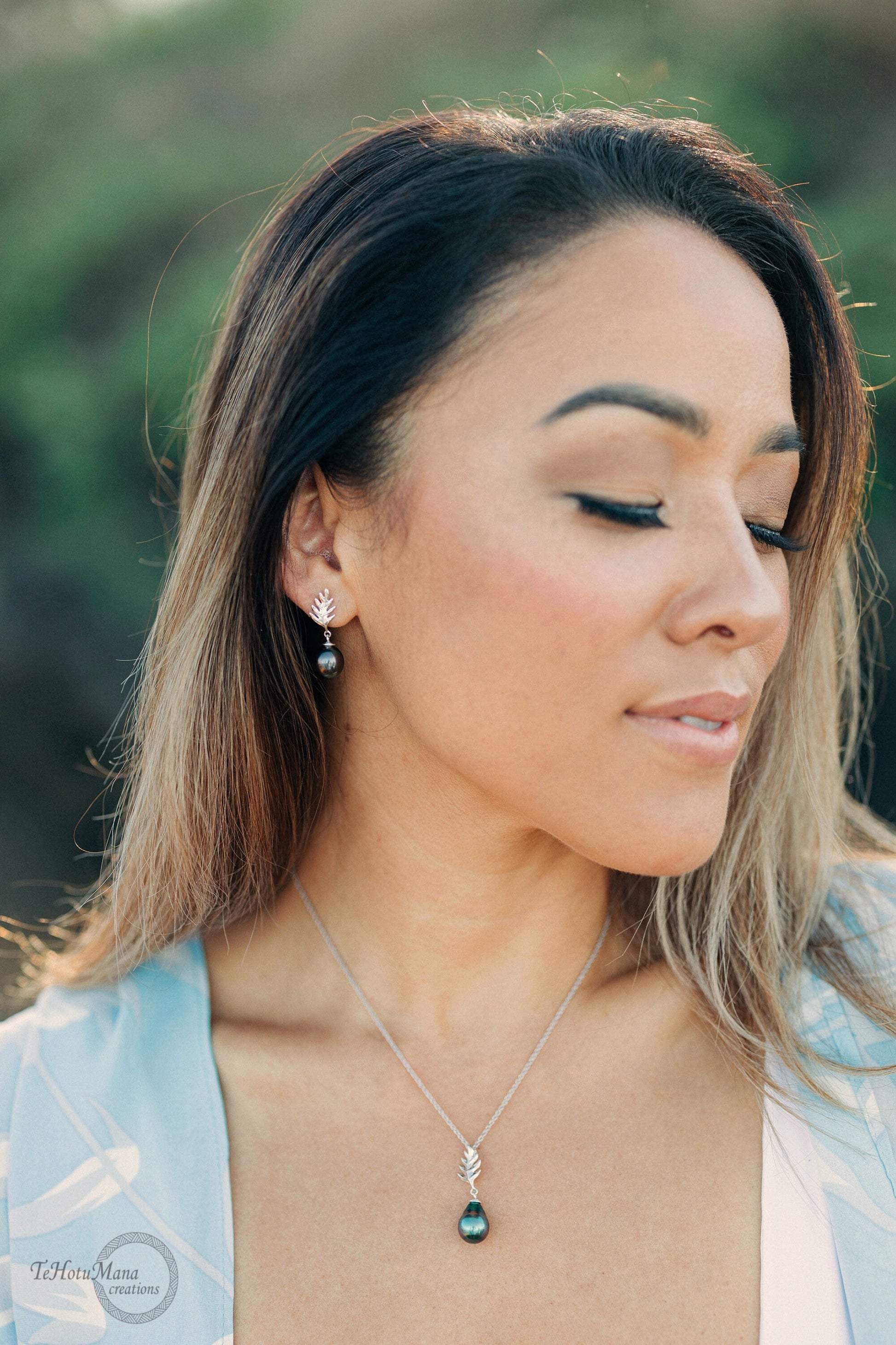 A silver necklace with a Tahitian black pearl and a Ulu leaf design. The necklace is paired with matching earrings with black pearls and leaf designs.