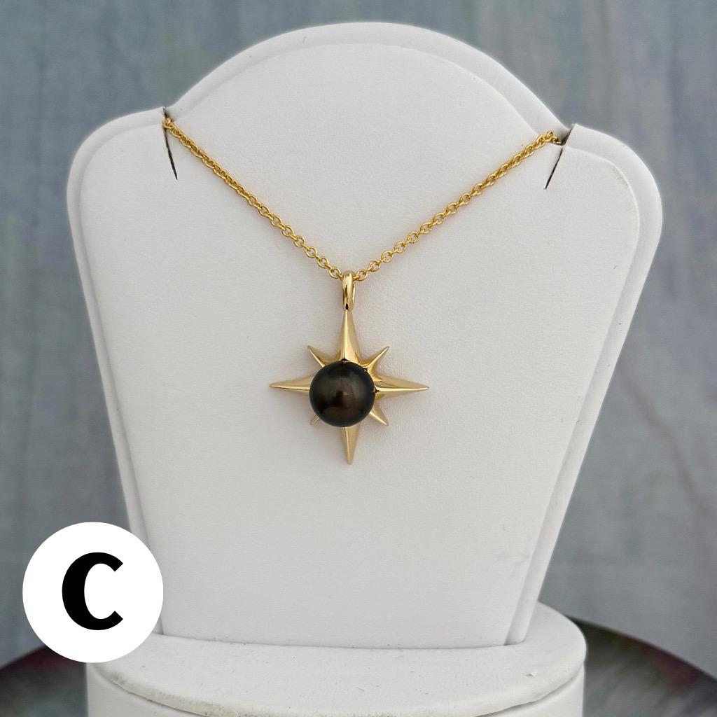 A gold-colored necklace featuring a starburst pendant with a dark, round center stone. The pendant is suspended from a delicate chain.