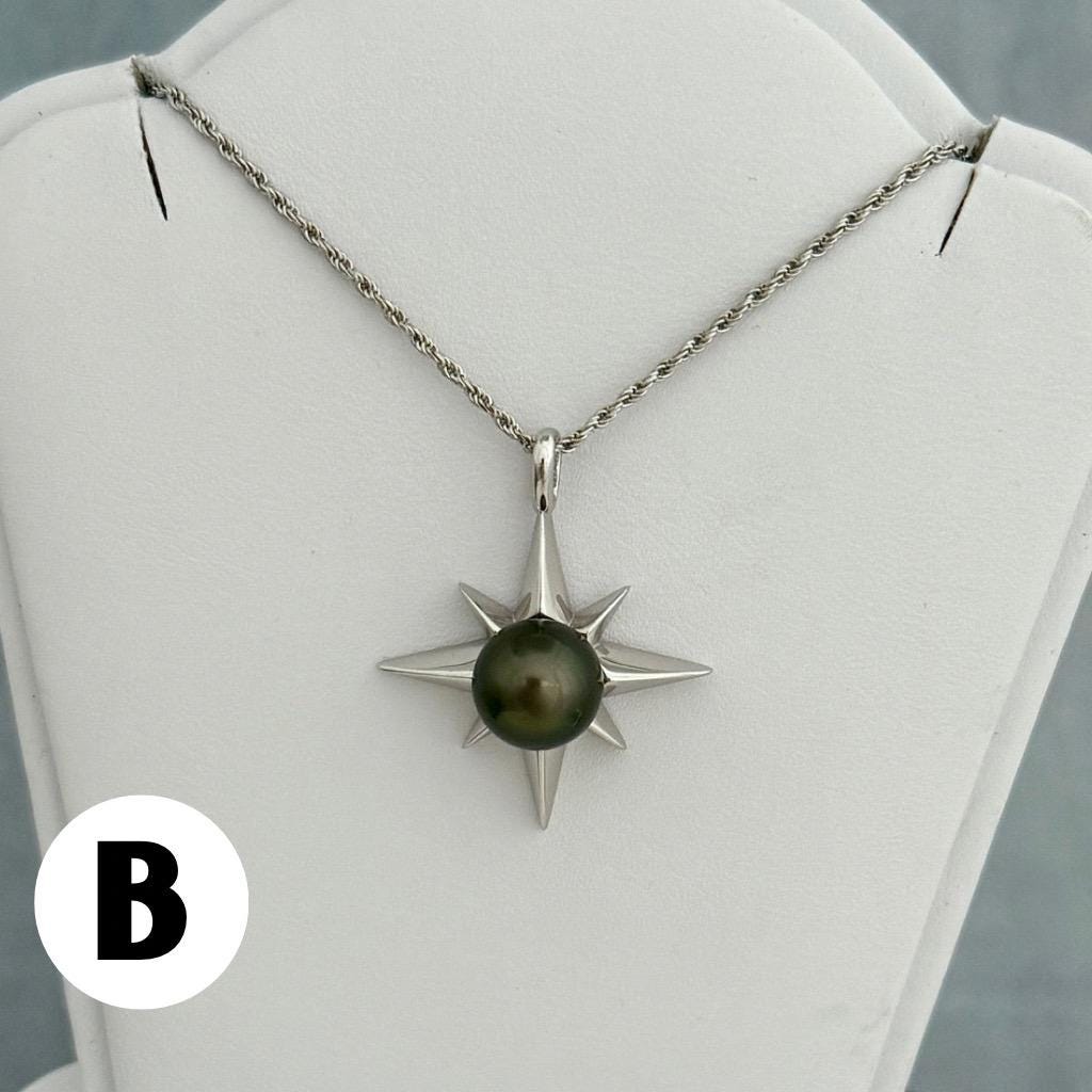 A silver-toned necklace featuring a starburst pendant with a dark green pearl at its center. The pendant is suspended from a delicate chain.