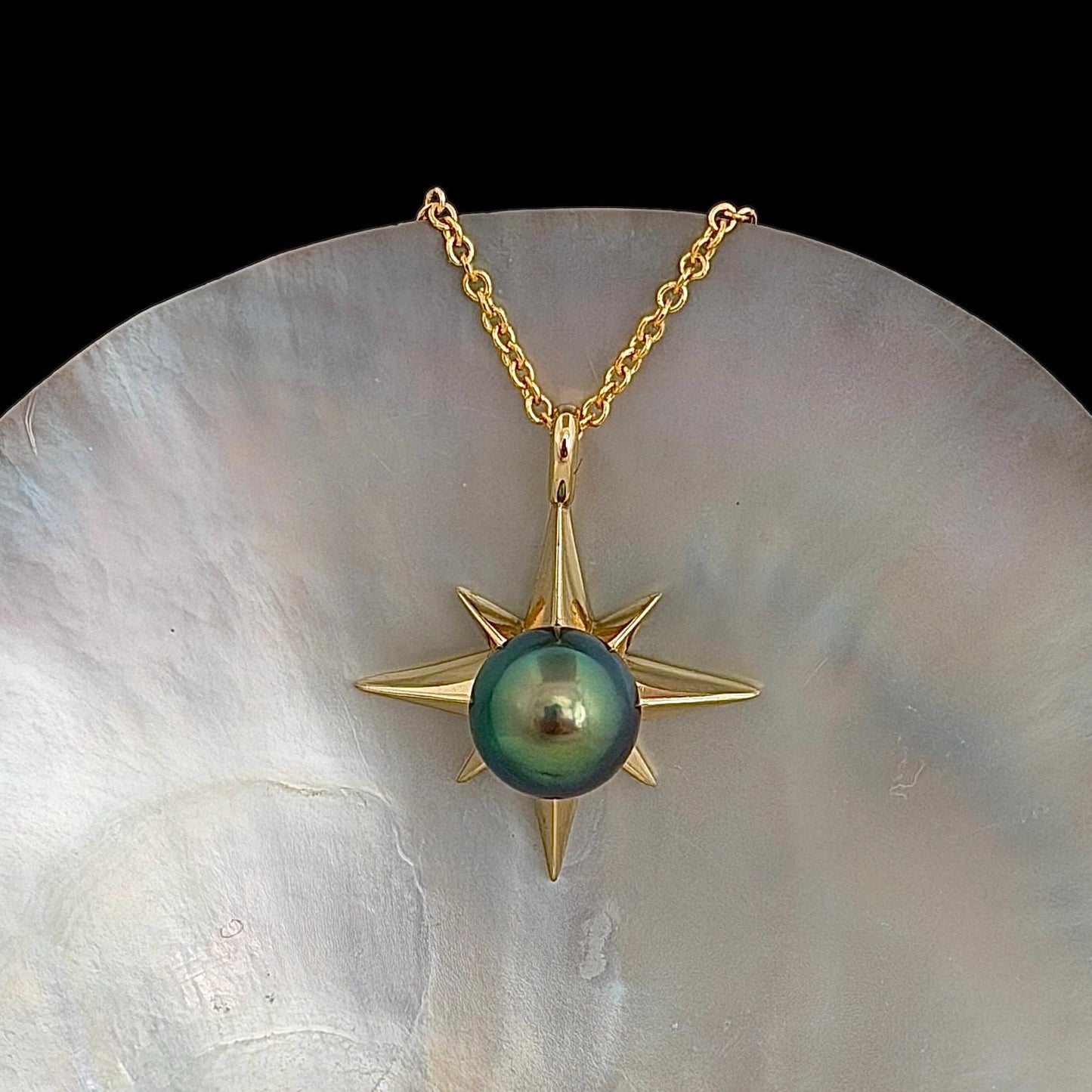 A gold-colored necklace featuring a starburst pendant with a vibrant blue green, round center stone. The pendant is suspended from a delicate chain.