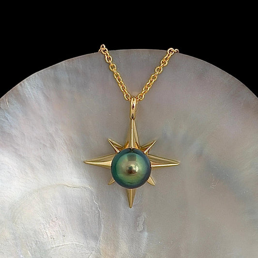 A gold-colored necklace featuring a starburst pendant with a vibrant blue green, round center stone. The pendant is suspended from a delicate chain.