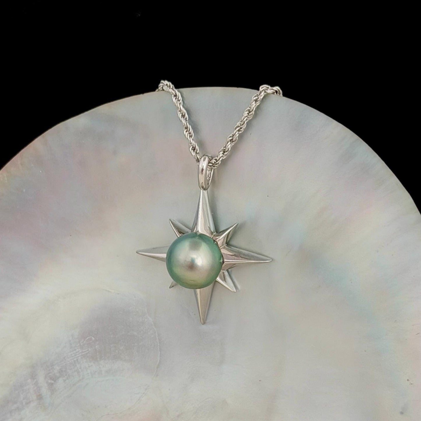 A silver-toned necklace featuring a starburst pendant with a pastel green pearl at its center. The pendant is suspended from a delicate chain.