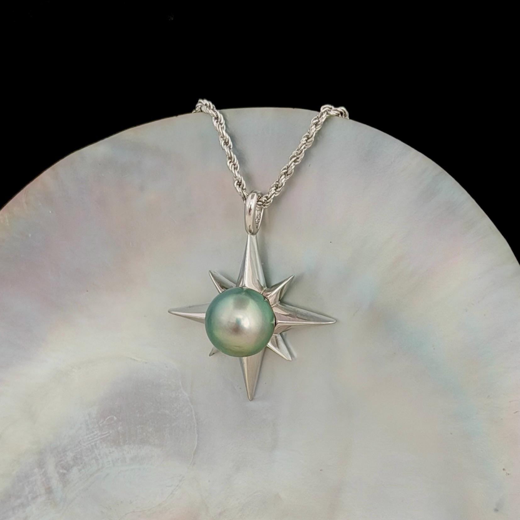 A silver-toned necklace featuring a starburst pendant with a pastel green pearl at its center. The pendant is suspended from a delicate chain.